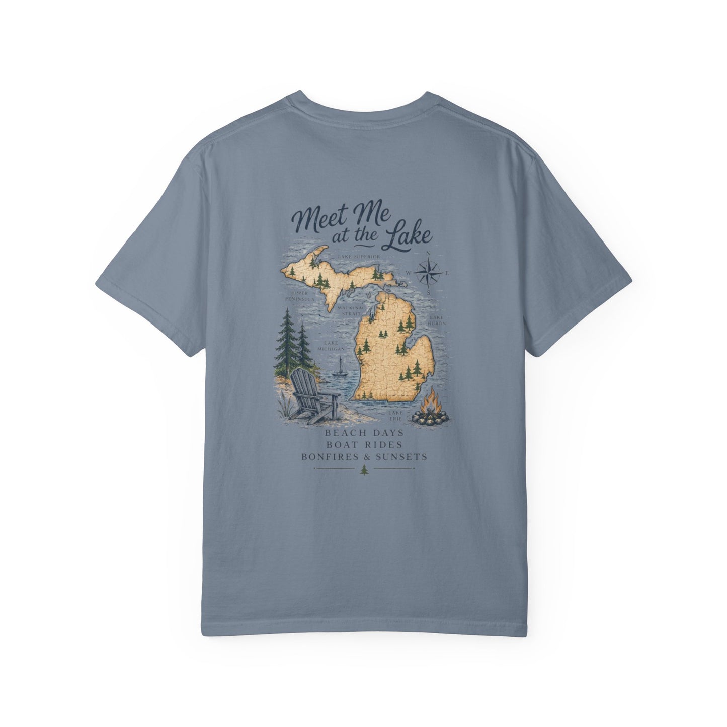 A slate blue short-sleeve t-shirt with a vintage-style map graphic of Michigan on the front, featuring the text 'Meet Me at the Lake' and outdoor elements like a campfire, trees, and a lake.