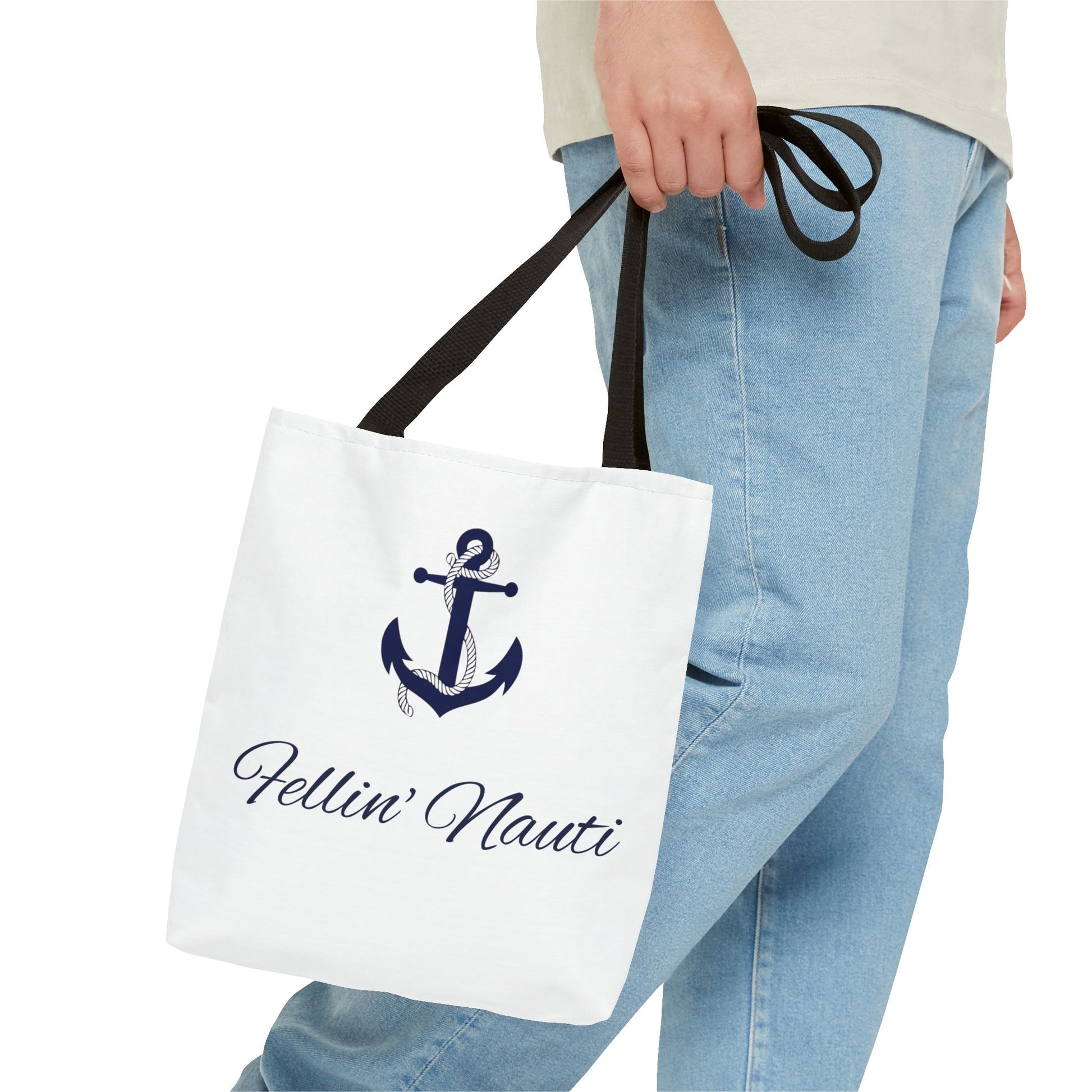 A white canvas tote bag with black handles, featuring a navy blue anchor graphic and the text 'Hellin' Nauti' in cursive, carried by a person wearing light blue jeans.