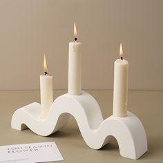 White wavy candle holder with three lit candles on a beige background
