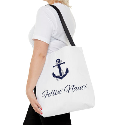 A white canvas tote bag with a black shoulder strap, featuring a navy blue anchor graphic and the text 'Fellin' Nauti' in cursive, shown being worn by a model.