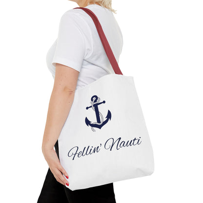 A white canvas tote bag with a dark blue anchor graphic and the text 'Fellin' Nauti' in script, carried on the shoulder of a model wearing a white t-shirt and black pants.