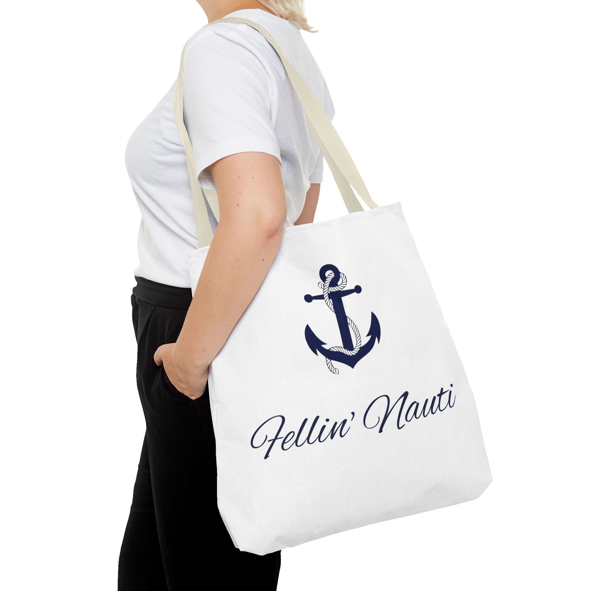 A person wearing a white t-shirt and black pants carries a white canvas tote bag with a navy blue anchor graphic and the text 'Fellin' Nauti' in cursive script.