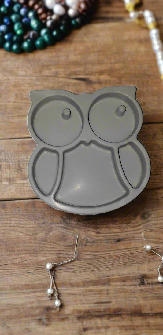 Gray owl-shaped dish on a wooden surface with jewelry items.