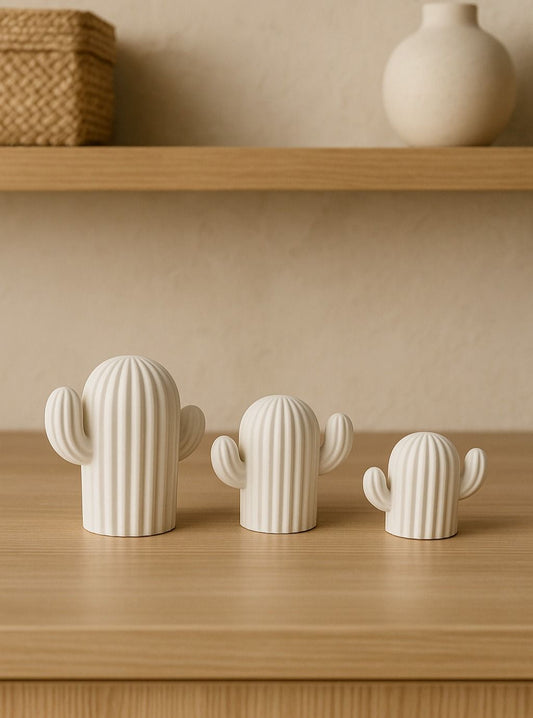 Three white ceramic cactus-shaped objects on a wooden surface with a beige wall in the background.