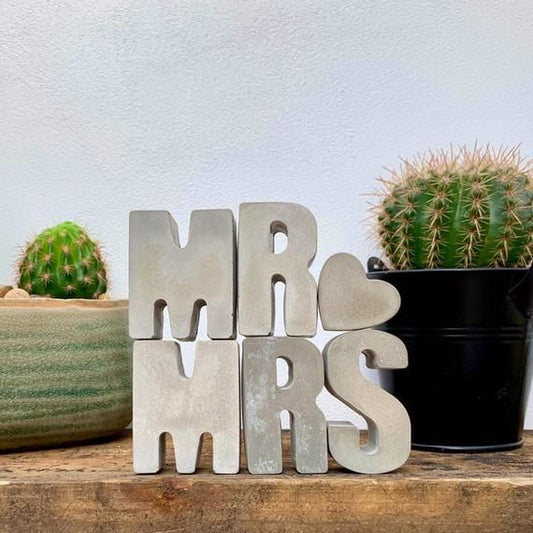Decorative sign with 'MR & MRS' letters between two cacti on a wooden surface.