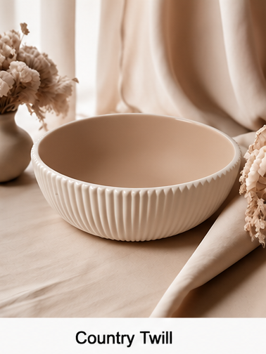 A cream-colored cement bowl with a ribbed, fluted exterior and a smooth, matte interior, styled on a beige fabric surface with dried flowers and draped curtains in the background. A white banner at the bottom has the text 'Country Twill'.
