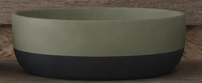 A two-tone cement bowl with a matte sage green upper half and a dark charcoal black lower half, set against a rustic wooden background.