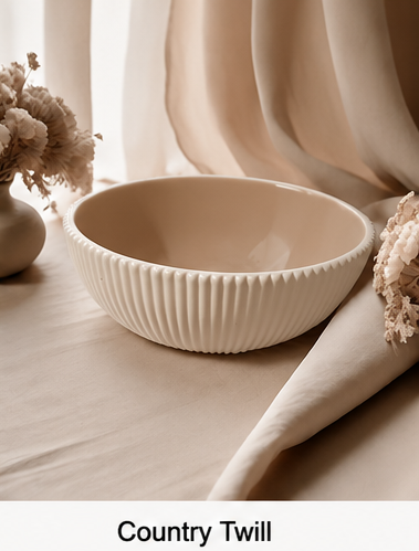 A cream-colored cement bowl with a ribbed fluted exterior and a smooth matte interior, styled on a beige fabric surface with draped cloth and dried flowers. Text at the bottom reads 'Country Twill'.