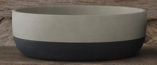 A round cement  bowl with a two-tone design, featuring a matte light beige upper half and a dark charcoal gray lower half, set against a rustic wooden background.