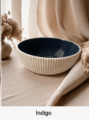 A ribbed cement bowl with a cream exterior and a deep indigo blue interior, styled on a beige fabric surface with dried flowers and draped curtains in the background.