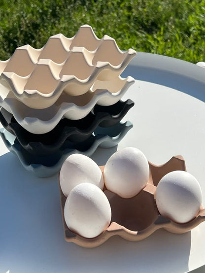 Stack of ceramic egg trays with eggs on a light surface