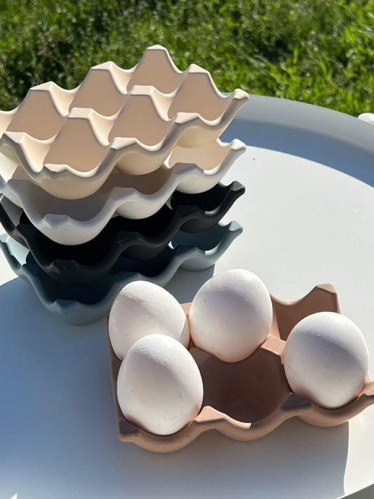 Stack of ceramic egg trays with eggs on a light surface