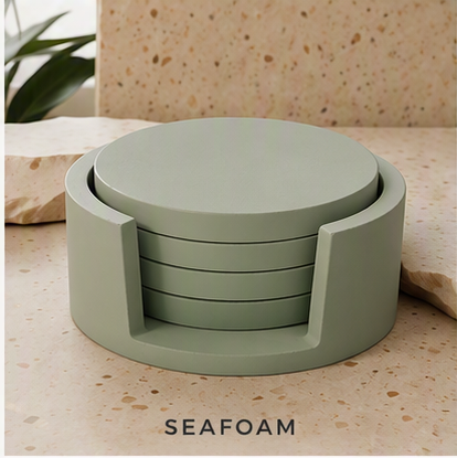 A set of round cement  coasters in a muted seafoam green color, displayed in a stack inside a matching circular holder on a speckled stone surface. The word 'SEAFOAM' is printed at the bottom.