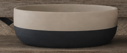 A two-tone cement bowl with a matte cream-colored upper half and a dark charcoal gray lower half, shown on a rustic wooden surface.