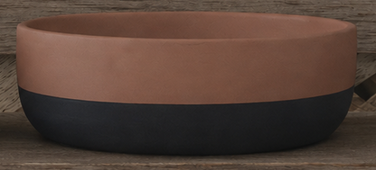 A two-tone cement bowl with a matte terracotta upper half and a dark charcoal black lower half, shown on a rustic wooden surface.