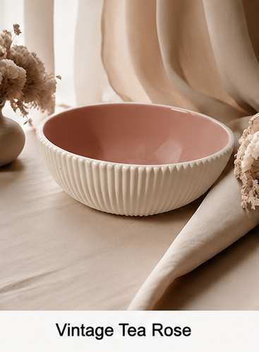 A cement bowl with a ribbed cream exterior and a dusty pink interior, labeled 'Vintage Tea Rose' at the bottom. The bowl is styled on a beige fabric surface with dried flowers and soft draped cloth in the background.