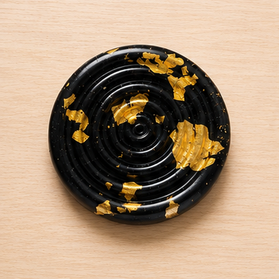 Black circular object with gold leaf on a beige background