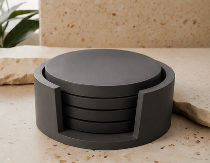 A dark charcoal gray circular cement coaster set with a matching top coaster, displayed on a beige stone surface with a matching stone background.