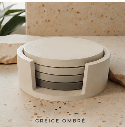 A round cement coaster set in a greige ombré finish, featuring a light beige outer ring and darker gray inner coasters, displayed on a matching speckled stone surface with the text 'GREIGE OMBRÉ' at the bottom.