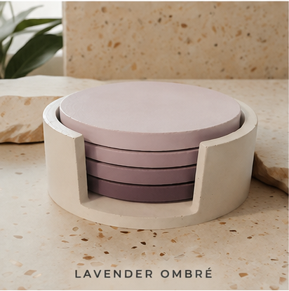 A set of four round cement coasters in a lavender ombré gradient, housed in a matching cream-colored cylindrical holder, displayed on a speckled stone surface.