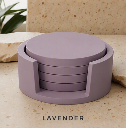 A set of round cement coasters in a muted lavender color, shown stacked inside a matching cylindrical holder on a beige stone surface with a plant in the background. The word 'LAVENDER' is printed below the product.