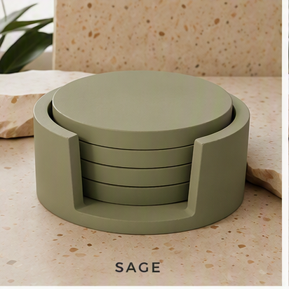 A sage green circular cement coaster set with a matching cylindrical holder, displayed on a beige speckled stone surface with the word 'SAGE' below.